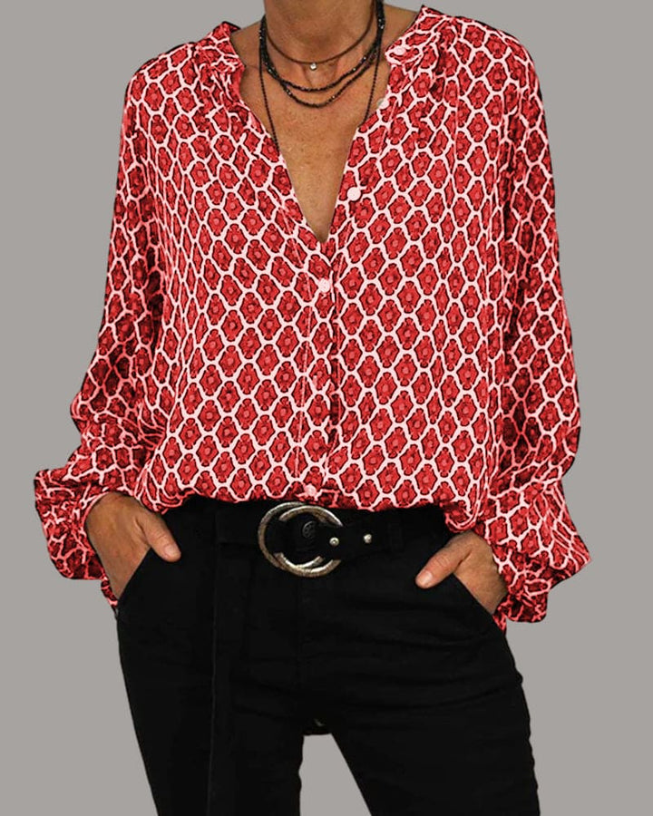 Women red geometric print long sleeve blouse with v-neck and button closure, styled with black pants.