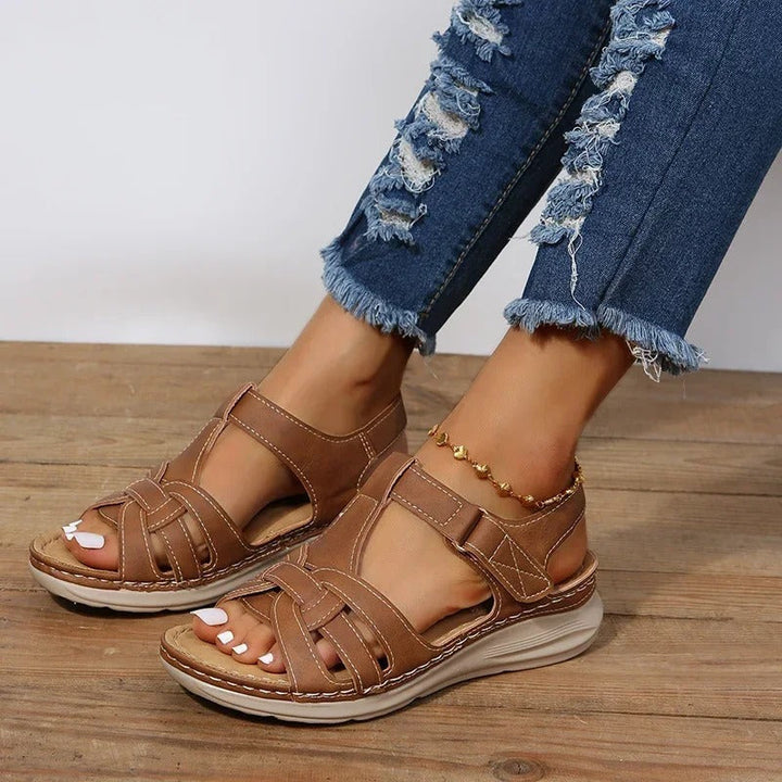 Women's brown strappy T-strap ankle sandals with contrast stitching on a wooden floor