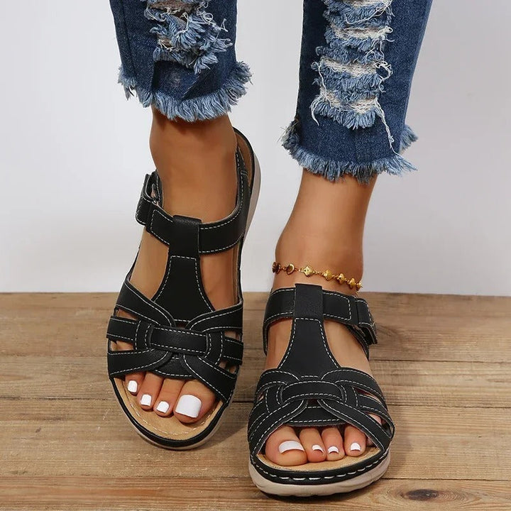 Women's black strappy T-strap sandals, front view showing buckle strap and white stitching