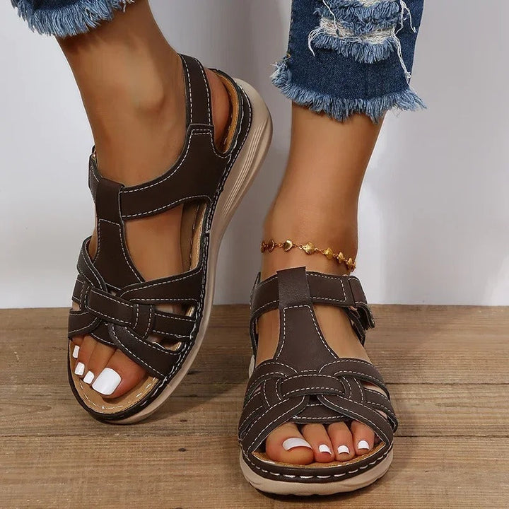 Women's dark brown strappy T-strap sandals, front view with white pedicure on bare feet
