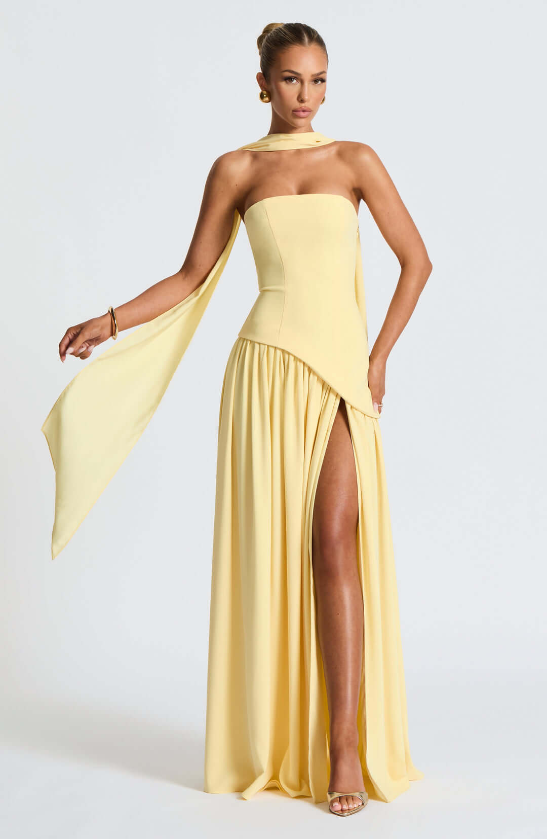 Women pale yellow strapless maxi dress with asymmetrical draped skirt and side split, front view.