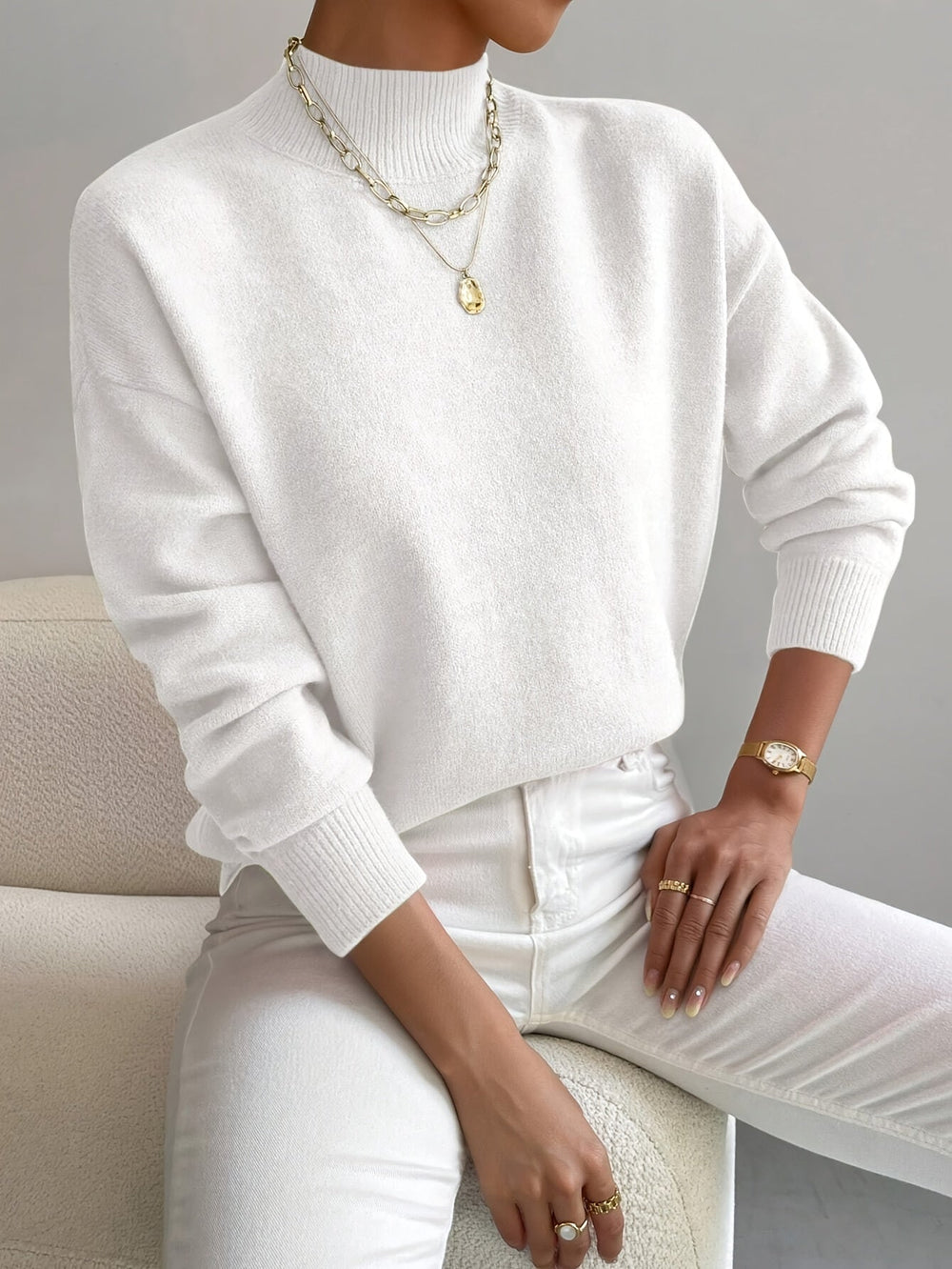 Women white turtleneck knit sweater with long sleeves and ribbed cuffs, seated pose.