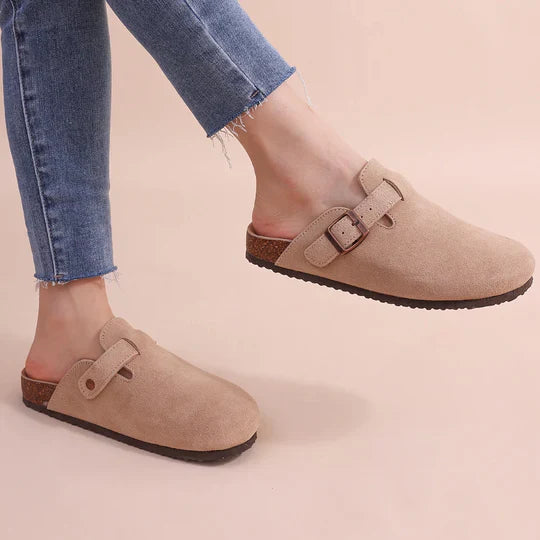 Women's tan suede-like cork buckle slide slippers worn on feet with blue jeans