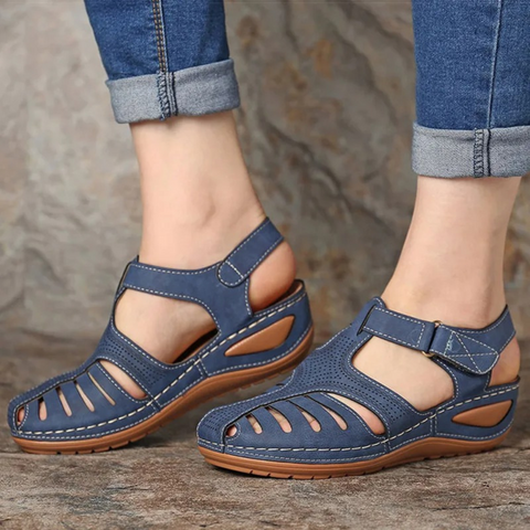 Women's blue strappy closed toe sandals with wedge heel and adjustable ankle strap on a model's feet