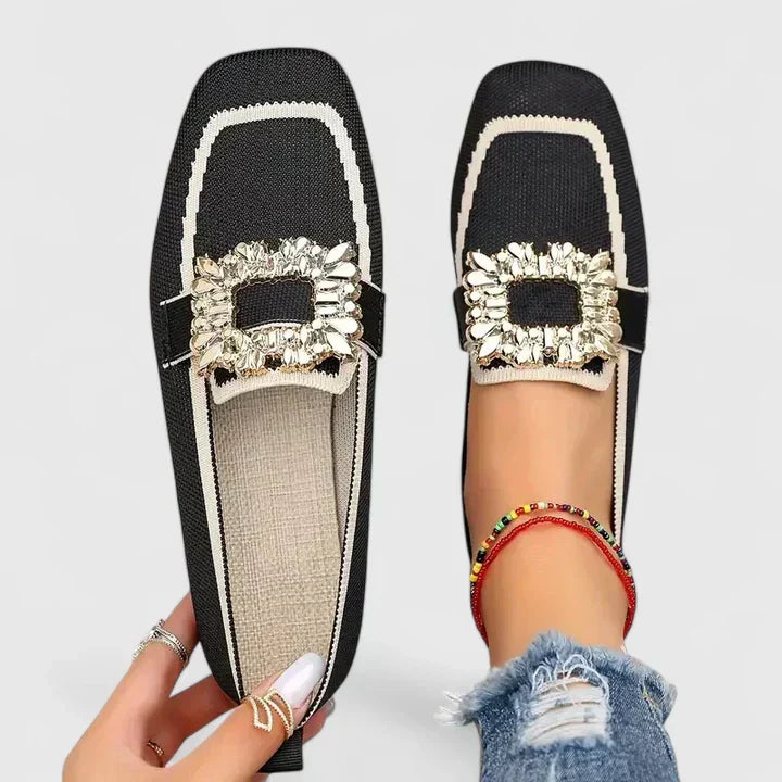 Black loafers with cream ruffled trim and gold decorative bow on foot