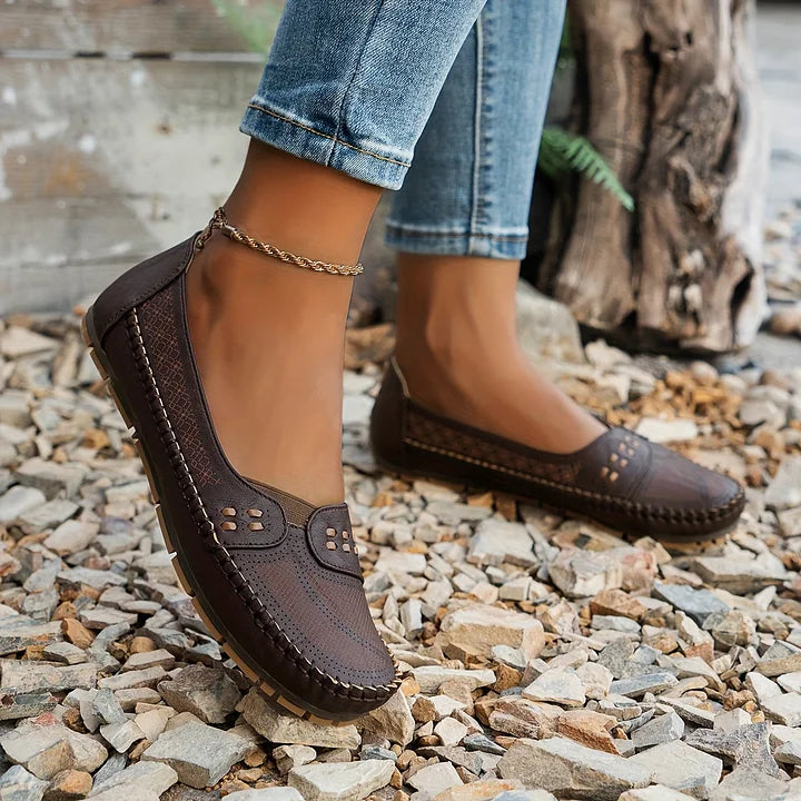 Dark brown perforated moc toe loafer flats with decorative studs on wearer